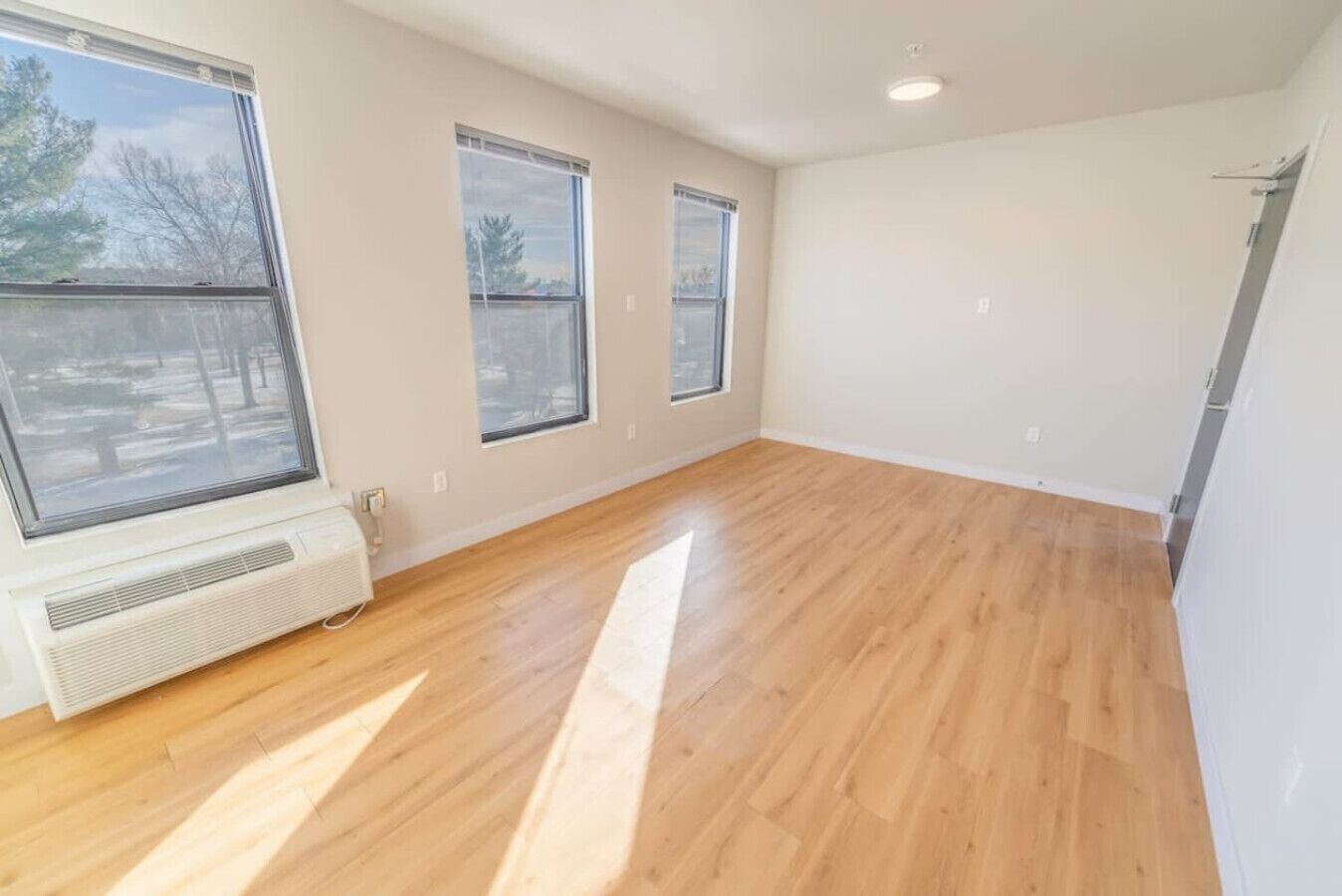 A spacious room with large windows, hardwood flooring, and white walls.