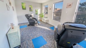Ein Zimmer mit Massagesessel, einem kleinen Tisch mit Pflanze und einem Fenster mit Blick auf die Stadt.
