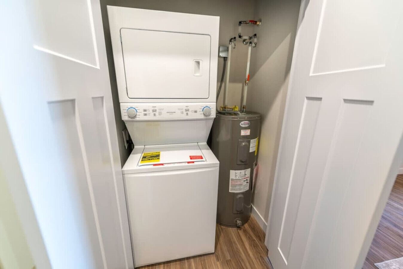 Une petite buanderie équipée d’un lave-linge et d’un sèche-linge à chargement frontal, d’un chauffe-eau et d’un petit panneau indicateur sur le sèche-linge.