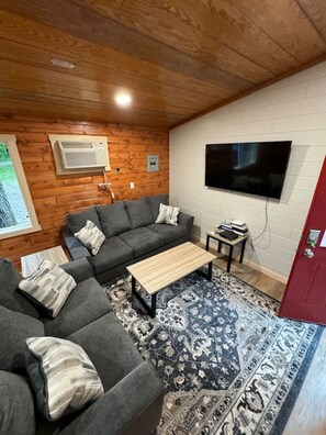 Ein gemütliches Wohnzimmer mit einem grauen Ecksofa, einem Holztisch und einem gemusterten Teppich.