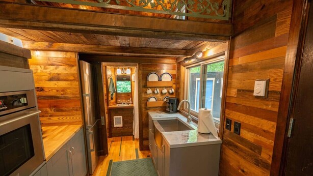 A compact kitchen with wooden walls, a built-in oven, a sink, and a coffee maker.