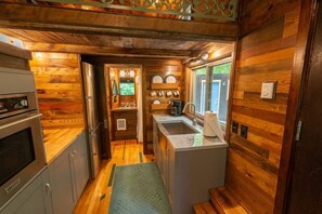 A compact kitchen with wooden walls, a built-in oven, a sink, and a coffee maker.