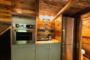 Una cocina compacta con horno de acero inoxidable, refrigerador y un colgador de cuchillos en la pared.