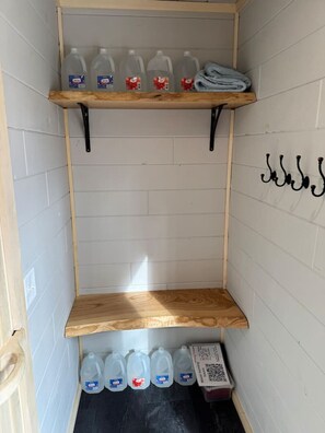 A corner storage area with wooden shelves holding plastic jugs and a folded towel.