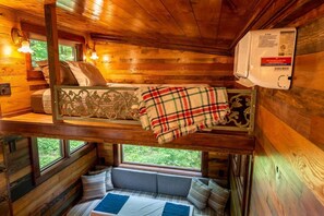 A cabin interior with a loft bed, a bench seat, and a window overlooking greenery. - River Retreat Tiny Homes:Wood Sauna/Rec Room/River (Willard)
