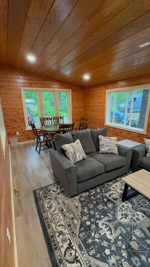 A cozy cabin interior with a gray sofa, a dining table, and a patterned rug.