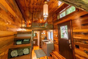 A wooden cabin interior with a kitchen, a bathroom, and a sleeping area.