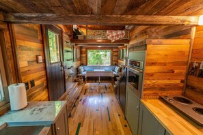 A compact kitchen with wooden walls, a central island, and a window providing a view of greenery.