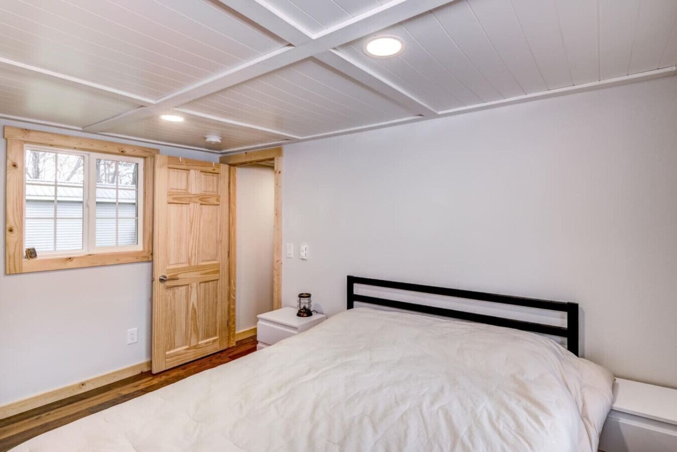A bedroom with a bed, a nightstand, a wooden door, and a window.