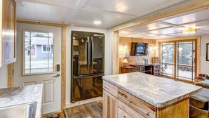 A compact kitchen with wooden cabinets, a marble countertop, and a large refrigerator. - Lake Holcombe Waterfront Escape (Holcombe)