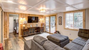 A cozy cabin interior with a wooden interior, a television mounted on the wall, and a large window providing a view of the outdoors. - Lake Holcombe Waterfront Escape (Holcombe)