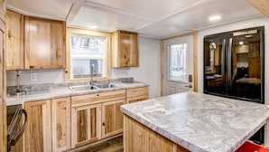 A kitchen with wooden cabinets, a marble countertop, and a black refrigerator. - Lake Holcombe Waterfront Escape (Holcombe)