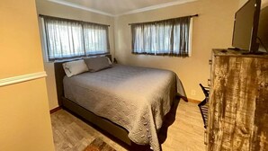 Una camera da letto con un letto, due finestre con tende, un comò in legno e una ventola a soffitto.