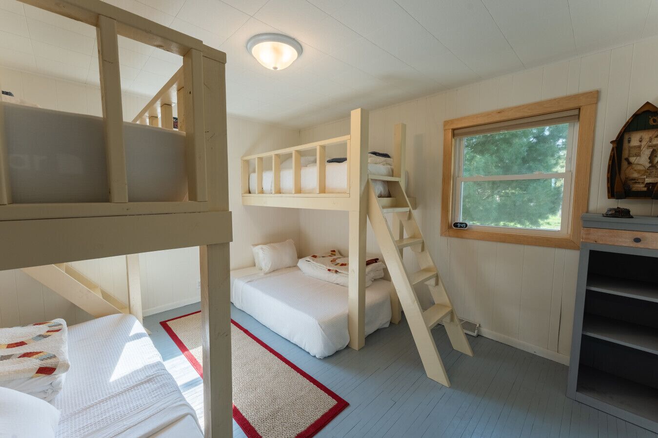 A room with bunk beds, a ladder, a window with a view, and a small desk with a clock.