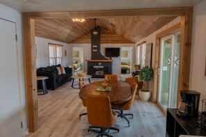 A spacious living area with a wooden ceiling, a round dining table with chairs, a sofa, and a fireplace.