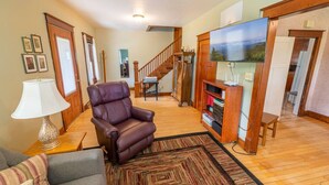 Una sala de estar con un sillón de cuero, un sofá, un tapete estampado, un televisor y una escalera que conduce a otra habitación.