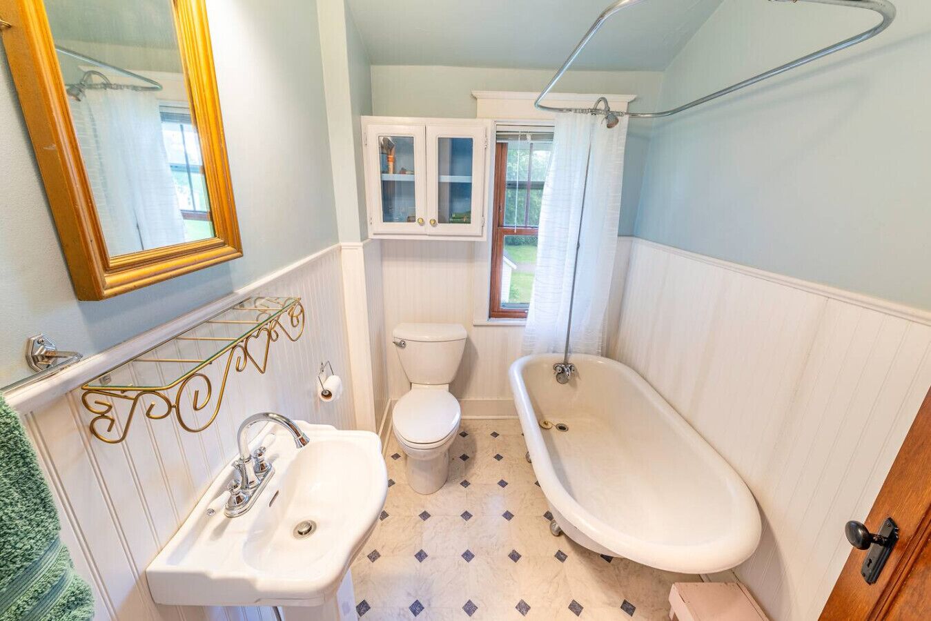 Ein Badezimmer mit weißem Waschbecken, Toilette und Badewanne. Ein Fenster bietet Blick auf Grünfläche draußen.