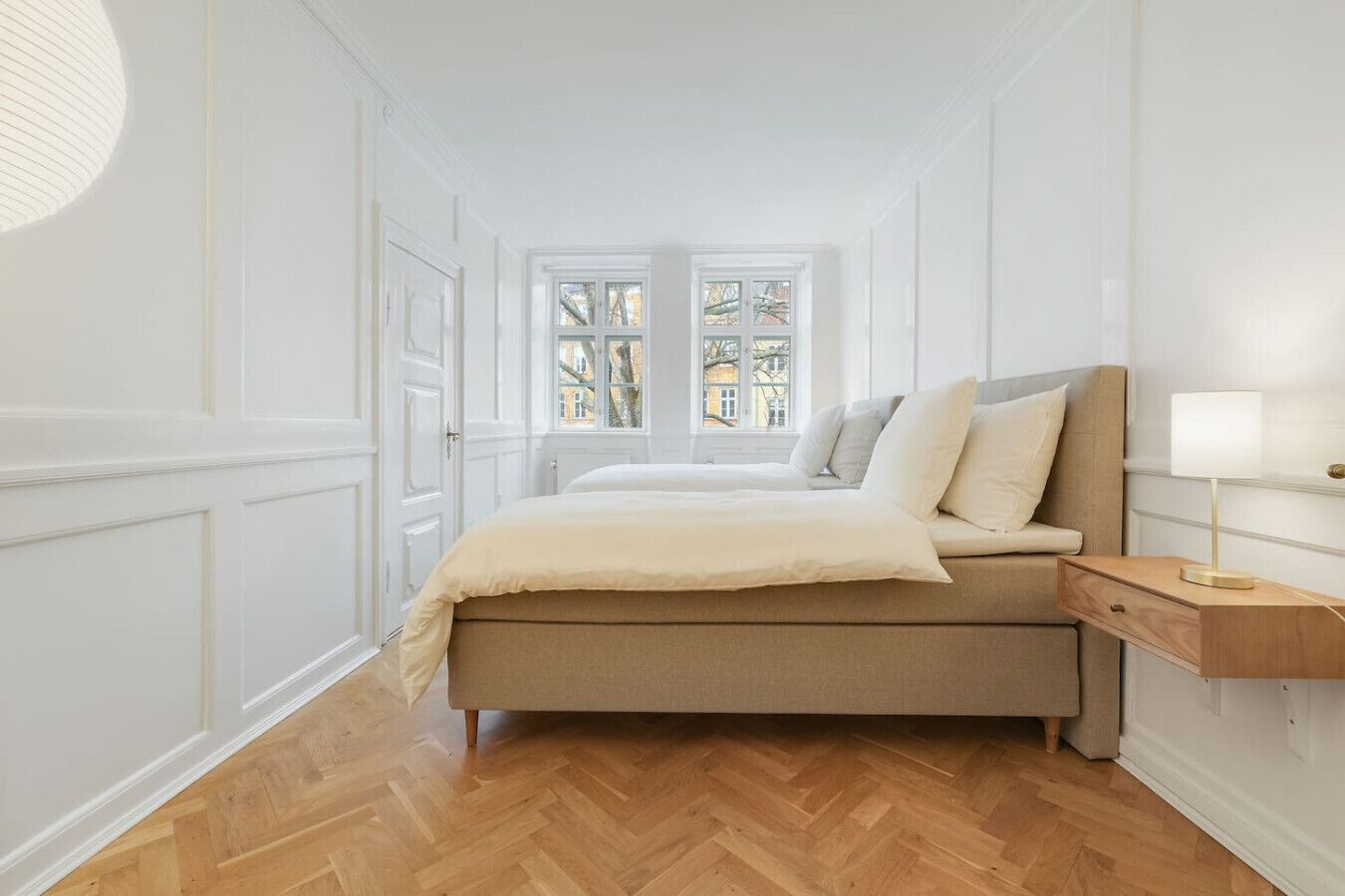 A bedroom with a bed, a nightstand, and a window with a view of buildings.