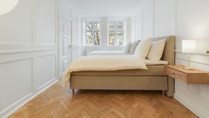 A bedroom with a bed, a nightstand, and a window with a view of buildings. - Beautiful apartment in the center of KBH (København)