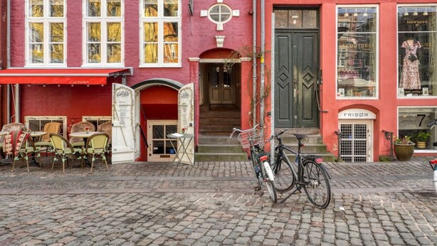A red building with a boutique on the ground floor and a restaurant with outdoor seating on the upper floor. - Beautiful apartment in the center of KBH (København)
