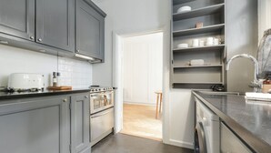 A modern kitchen with grey cabinets, a built-in oven, a toaster, and a coffee machine. There is a dining area visible through an open door. - Beautiful apartment in the center of KBH (København)