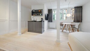 A modern, well-lit room with a kitchenette, a dining area, and a large window with curtains. - Small apartment in the heart of KBH (København)