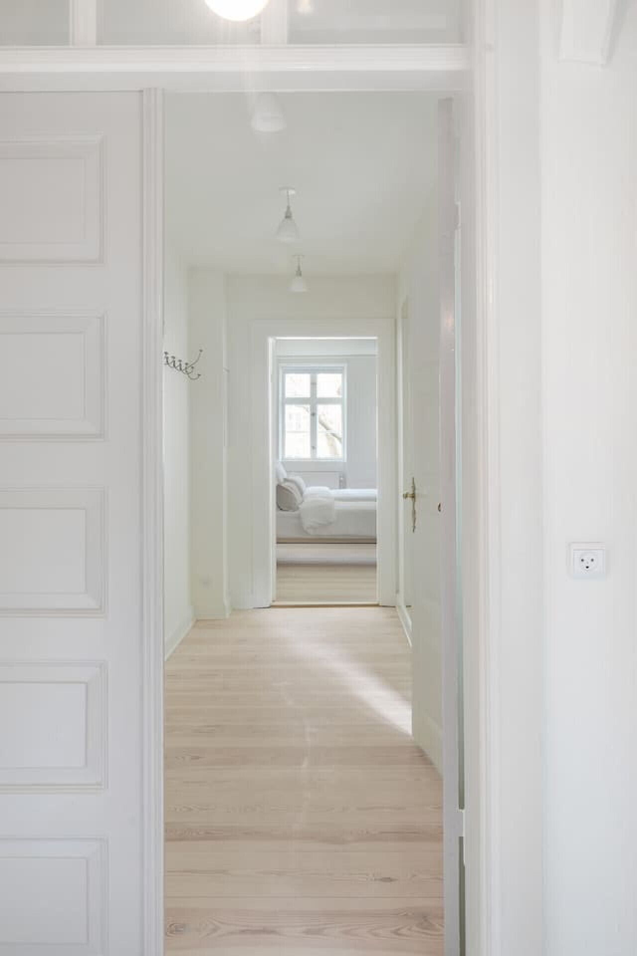 Een gang die leidt naar een slaapkamer met een bed, een raam en een plafondlamp.