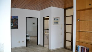 A hallway with a tiled floor, a wooden door, and a bookshelf with books. - PentArtHouse Apartment (Burscheid)