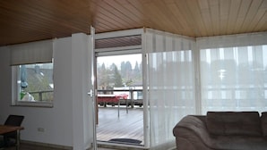 A room with a wooden ceiling, a sliding glass door leading to an outdoor deck, a brown sofa, and a small table. - PentArtHouse Apartment (Burscheid)