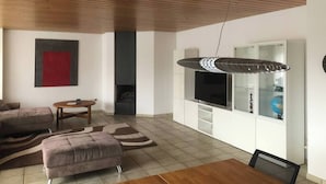 A modern living room with a wooden ceiling, a flat-screen TV, a sofa, a coffee table, and a patterned rug. - PentArtHouse Apartment (Burscheid)