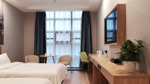 A hotel room with two beds, a desk, a chair, a TV, and a window with curtains.