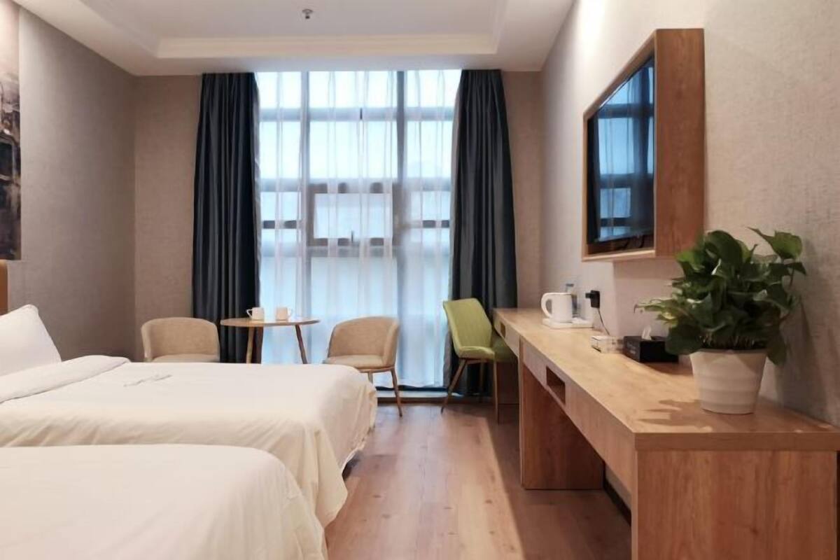 A hotel room with two beds, a desk, a chair, a TV, and a window with curtains.