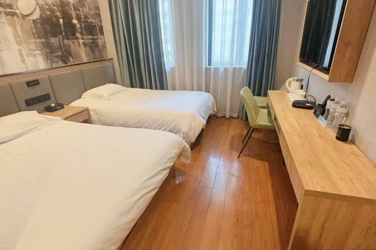 A hotel room with two beds, a wooden desk, a chair, a TV, and a window with curtains.