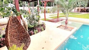 A pool area with a hanging chair, a small palm tree, and a wooden deck. - Peaceful House, Private Pool, 2 cars included (Akumal)