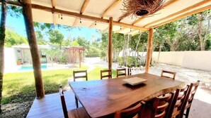 An outdoor wooden table with chairs under a pergola, surrounded by greenery and a clear sky. - Peaceful House, Private Pool, 2 cars included (Akumal)