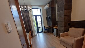 A modern living room with a sofa, a small table, and a TV. There is a door leading to another room and a window with curtains. - Old Avenue Hotel (Gyumri)