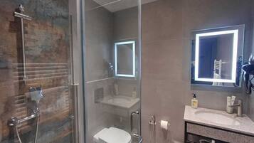 Un bany modern amb dutxa de vidre, vàter i un lavabo amb mirall.
