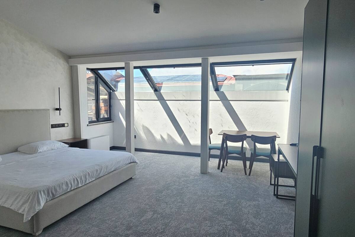 Une chambre à coucher avec un lit, un bureau et une chaise. Une grande fenêtre offre une vue sur la plage.
