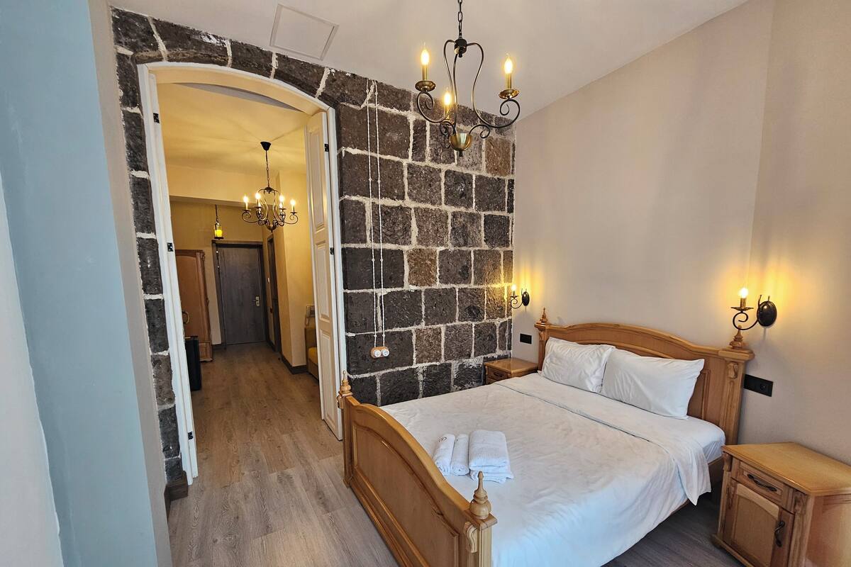 Une chambre avec un mur en pierre, un lit en bois, une table de chevet et une armoire en bois.