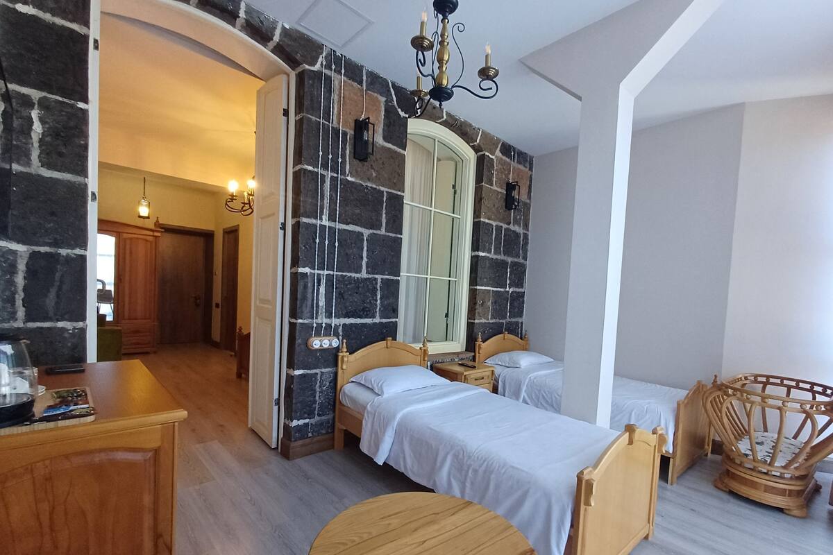 Une pièce chaleureuse avec deux lits en bois, une table ronde en bois et un mur de pierre agrémenté d’une fenêtre.