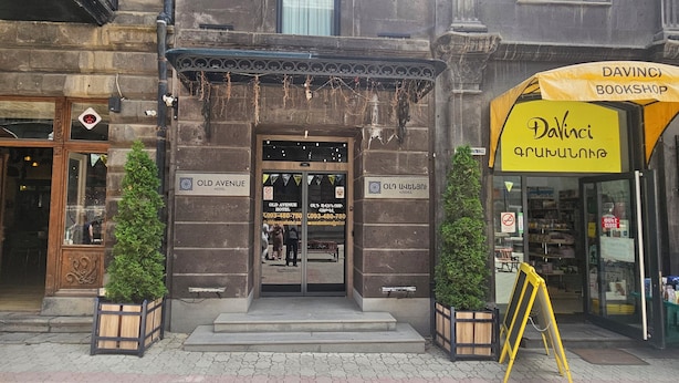 The entrance to the Old Avenue Hotel with a signboard, a wooden door, and a yellow Davinci Bookshop to the right. - Old Avenue Hotel (Gyumri)