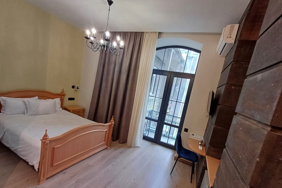 Une chambre à coucher avec un lit en bois, un lustre, un bureau avec une chaise et une grande fenêtre avec des rideaux.