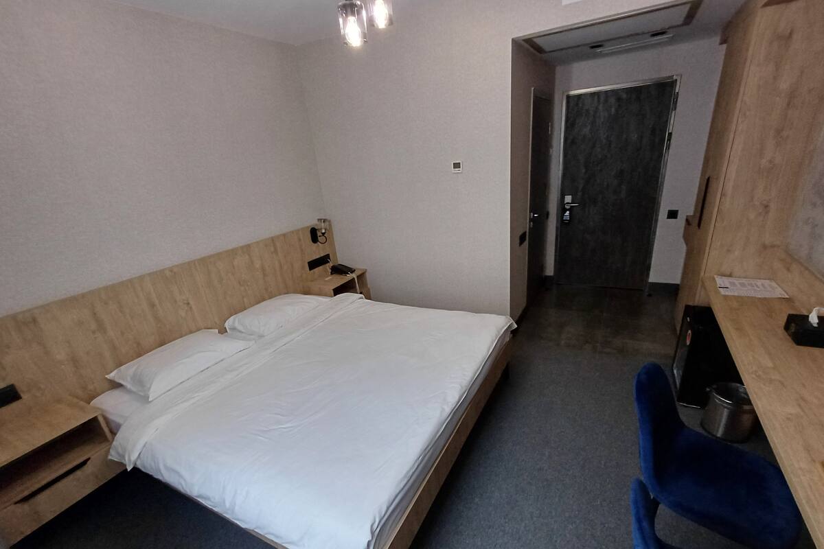 Une chambre d’hôtel avec un lit en bois, un bureau avec une chaise, une petite table et une porte donnant sur une autre pièce.