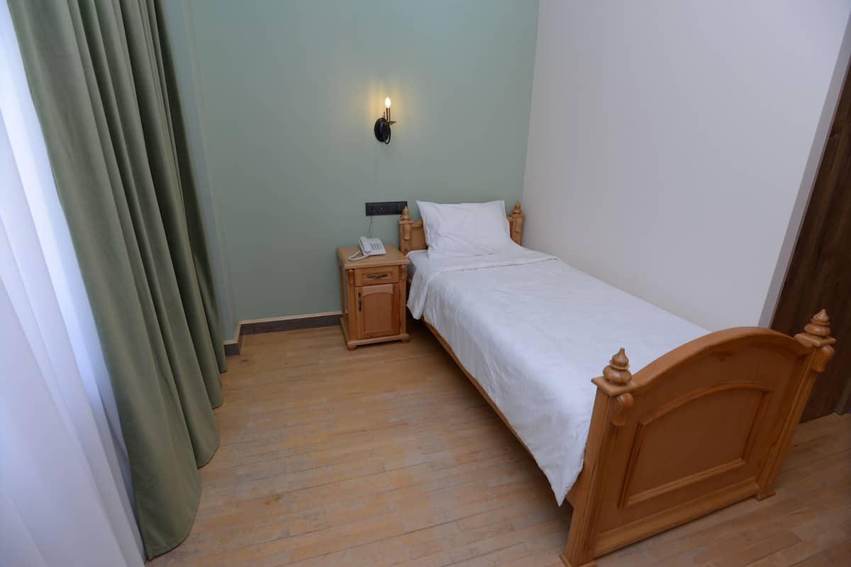 Une chambre à coucher avec un lit en bois, une table de chevet avec un téléphone et un luminaire fixé au mur.