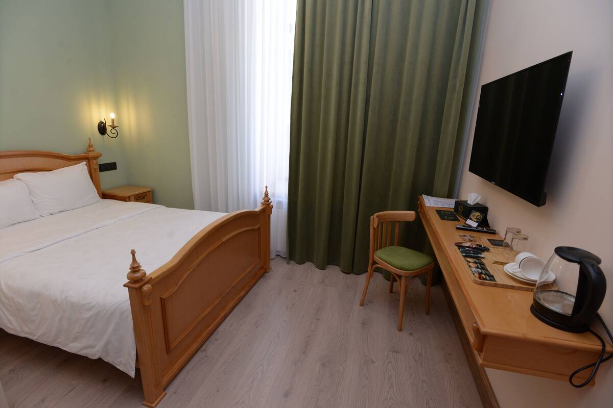 Une chambre d’hôtel avec un lit en bois, un bureau avec une chaise, un téléviseur à écran plat et une fenêtre avec des rideaux.