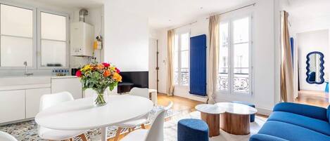 A modern living room with a dining area, a blue sofa, and a kitchen with white cabinets.