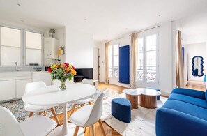 Ein modernes Wohnzimmer mit Essbereich, einem blauen Sofa und einer Küche mit weißen Schränken.