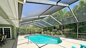 An outdoor swimming pool with a covered area, surrounded by greenery and equipped with blue chairs. - 2Bd 2Ba Get Away In The Prestigious Meadows Community! Golf, Tennis, and More! (Sarasota)