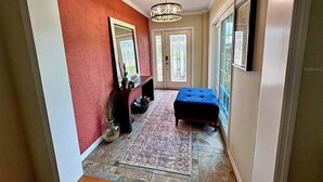 A hallway with a red wall, a wooden bench, a rug, and a chandelier. - 2Bd 2Ba Get Away In The Prestigious Meadows Community! Golf, Tennis, and More! (Sarasota)