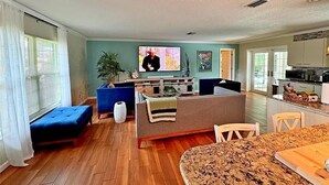 A modern living room with a blue sofa, a dining table, and a kitchen area in the background. - 2Bd 2Ba Get Away In The Prestigious Meadows Community! Golf, Tennis, and More! (Sarasota)